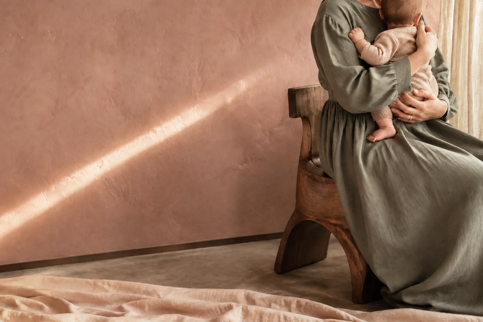 A parent holding their baby beside a warm blush wall